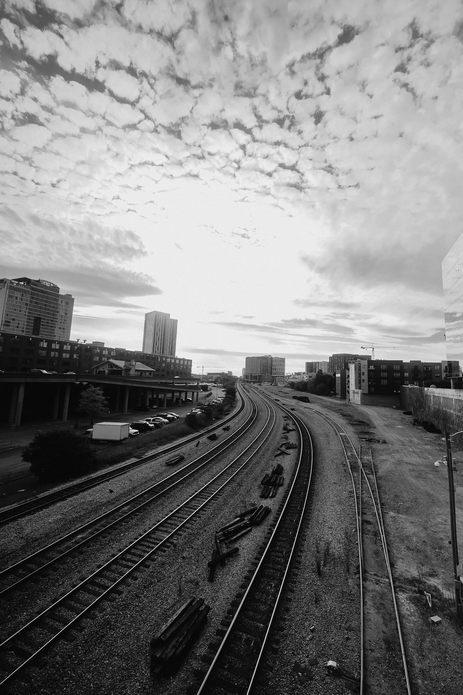 Railway tracks curving out of a city under a mottled sky. Photo by Jordan Ryskamp.