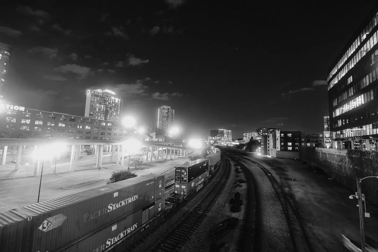 A freight train stacked with shipping containers beside a city at night. Photo by Jordan Ryskamp.
