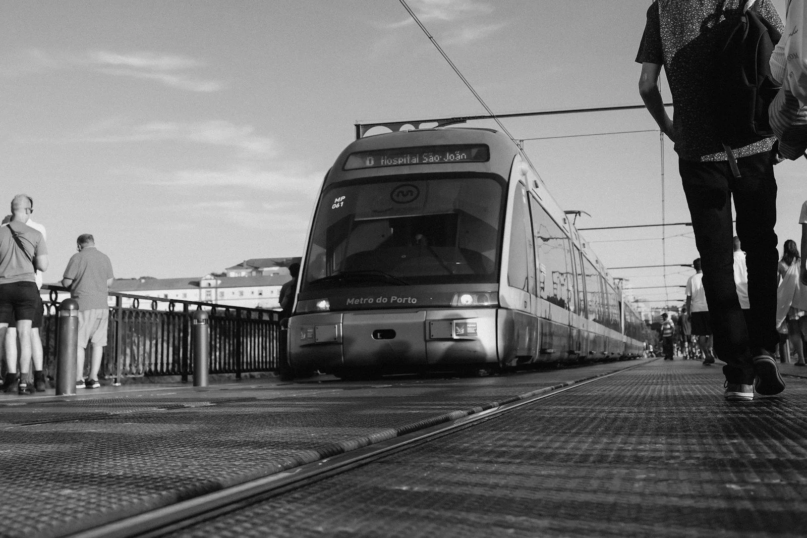 A Porto light-rail train arriving on a bridge as people walk beside the tracks. Photo by Jordan Ryskamp.